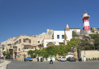 Cars on road by buildings against clear blue sky