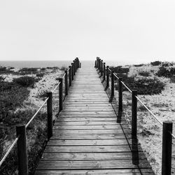 Empty wooden pier leading towards sea against clear sky