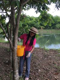 Full length of woman holding bucket standing by tree 