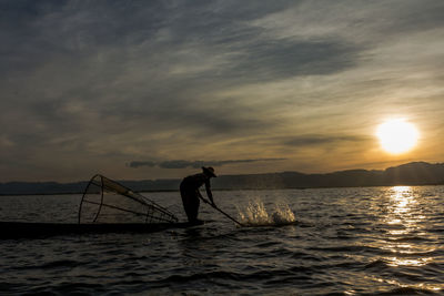 Silhouette man fishing in sea against sunset sky