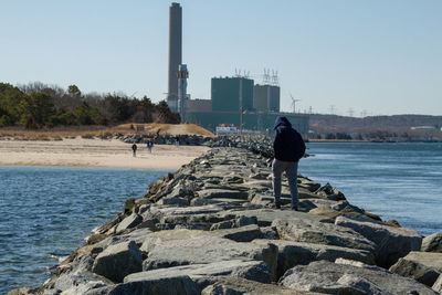 Rear view of man on rock by sea against clear sky