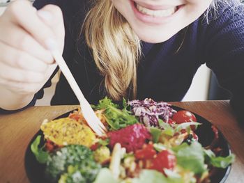 Midsection of happy woman eating salad at table