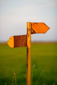 Close-up of road sign on field against sky