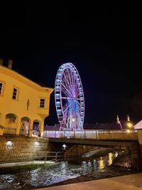 Illuminated ferris wheel in city against sky at night