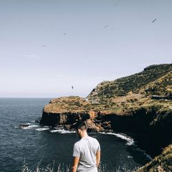 Rear view of man standing by sea and mountain against clear sky