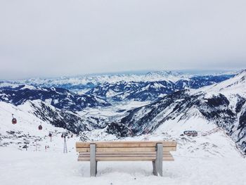 Empty bench on snowcapped mountain against sky
