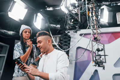 Young man is preparing for tv online broadcast. woman helps with make up.