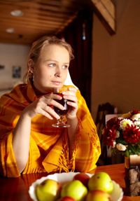 Thoughtful woman looking away while having drink at home