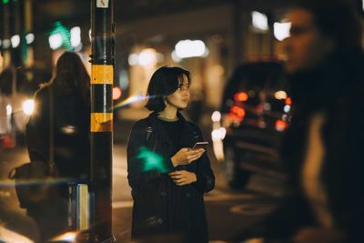 Young woman looking away while using cellphone in city at night