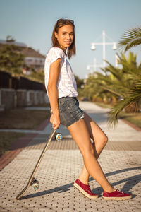 Beautiful young girl with skateboard posing on the street in a sunny summer day