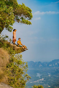 Men sitting on tree by mountain against sky
