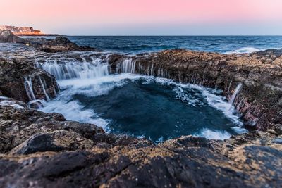 Scenic view of waterfall and rocky mountains during sunset