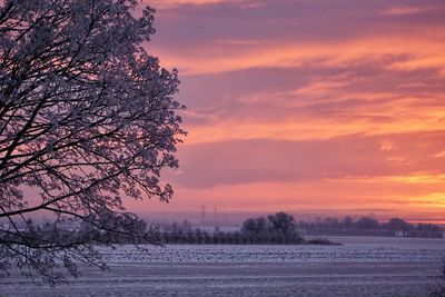 Snow covered field against sky during sunset