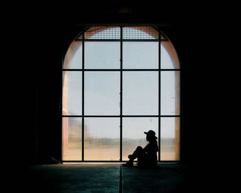 Side view of a silhouette man sitting against window in building