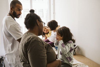 Male pediatrician and woman looking at girl covering eyes sitting with playful sisters