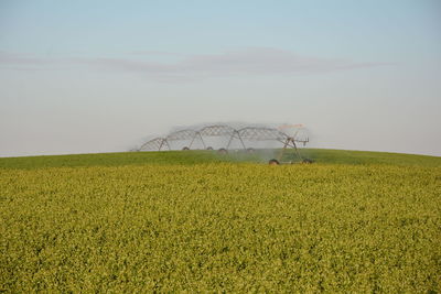 Agricultural sprinkler spraying water on field against sky