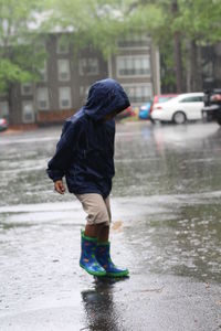 Boy in raincoat standing on street during rainfall