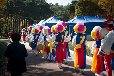 Rear view of people wearing colorful costume while dancing on street against trees