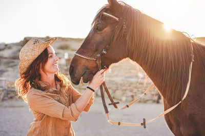 Smiling woman holding horse saddle against clear sky