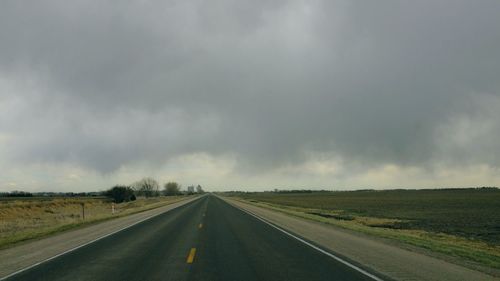 Road passing through landscape against storm clouds