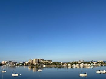 Sailboats in city at harbor against clear blue sky