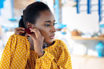 Portrait of beautiful african american model girl in yellow dress puts on jewelry earrings 