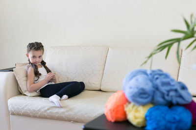 Portrait of smiling girl with wool sitting on sofa at home