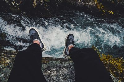 Low section of man sitting on rock over waterfall