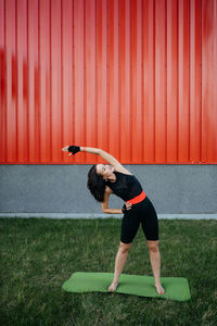 Young brunette woman of thirty is doing stretching exercises on the green grass in the park.