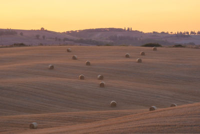 Hay bales on field against sky during sunset