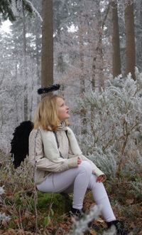 Young woman wearing costume wing and halo sitting on rock at forest during winter