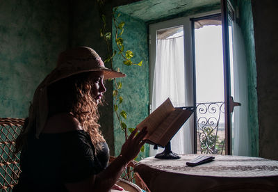 Woman reading book while sitting by table at home