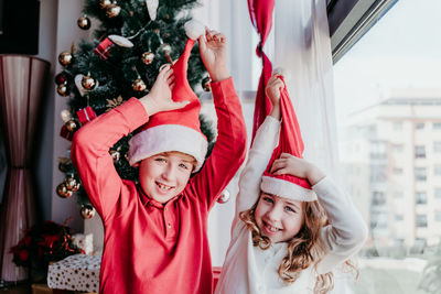 Portrait of siblings wearing santa hats while standing at home