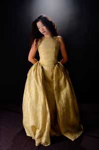 Woman wearing golden dress standing against black background