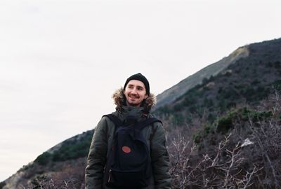 Young man with backpack standing by mountain against clear sky