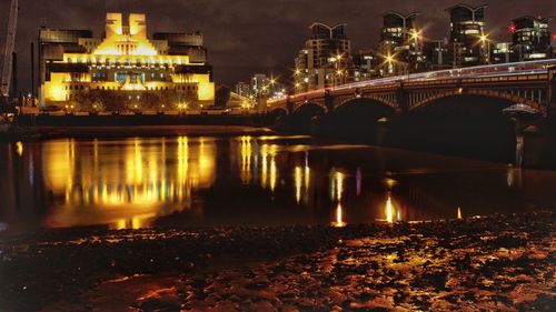 Illuminated bridge over river by city at night