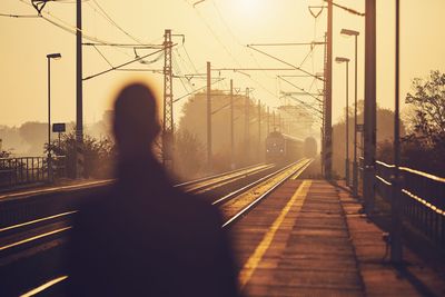 Rear view of man at railroad station against sky