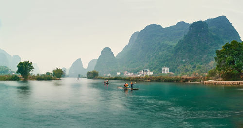 People on river by mountains against clear sky