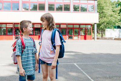 Boy and a girl, brother and sister stand with backpacks on their backs in front of the school 