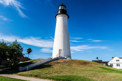 Low angle view of lighthouse on grassy field against blue sky