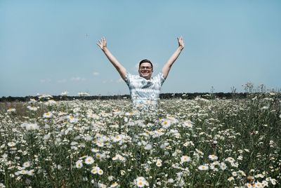 Man with arms outstretched standing amidst daisy flowers blooming on field