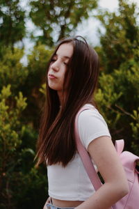 Side view of a beautiful young woman standing against trees