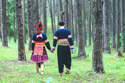 Rear view of friends standing by tree trunk in forest