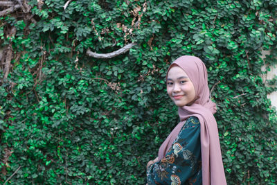 Portrait of young woman standing against plants