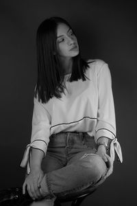 Beautiful young woman sitting against black background