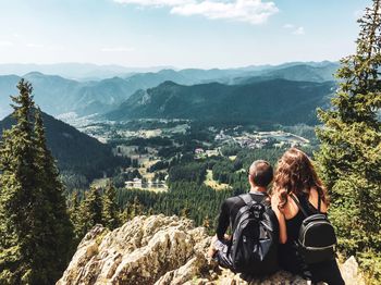 Rear view of couple sitting on cliff against sky