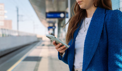 Midsection. young stylish woman using mobile while waiting for train at station. public transport.