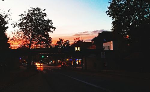 Road by silhouette trees against sky at sunset