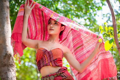 Woman holding scarf while standing against trees 