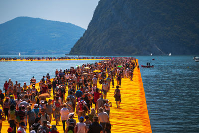 People on boardwalk in sea against mountains 